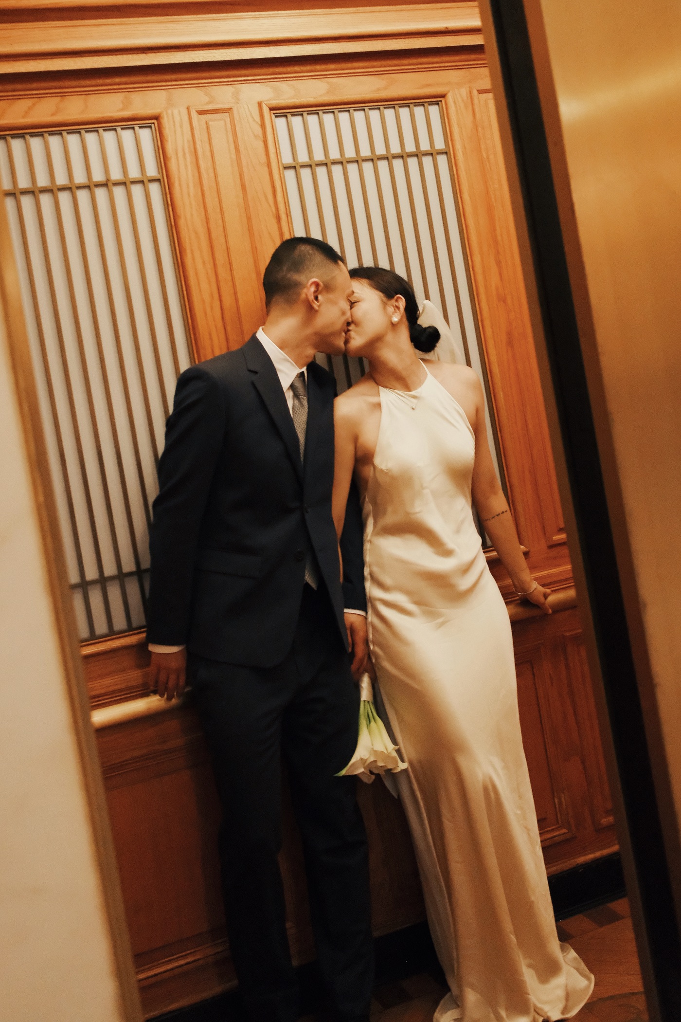 A newly married couple kissing in the warm wood interior of an elevator