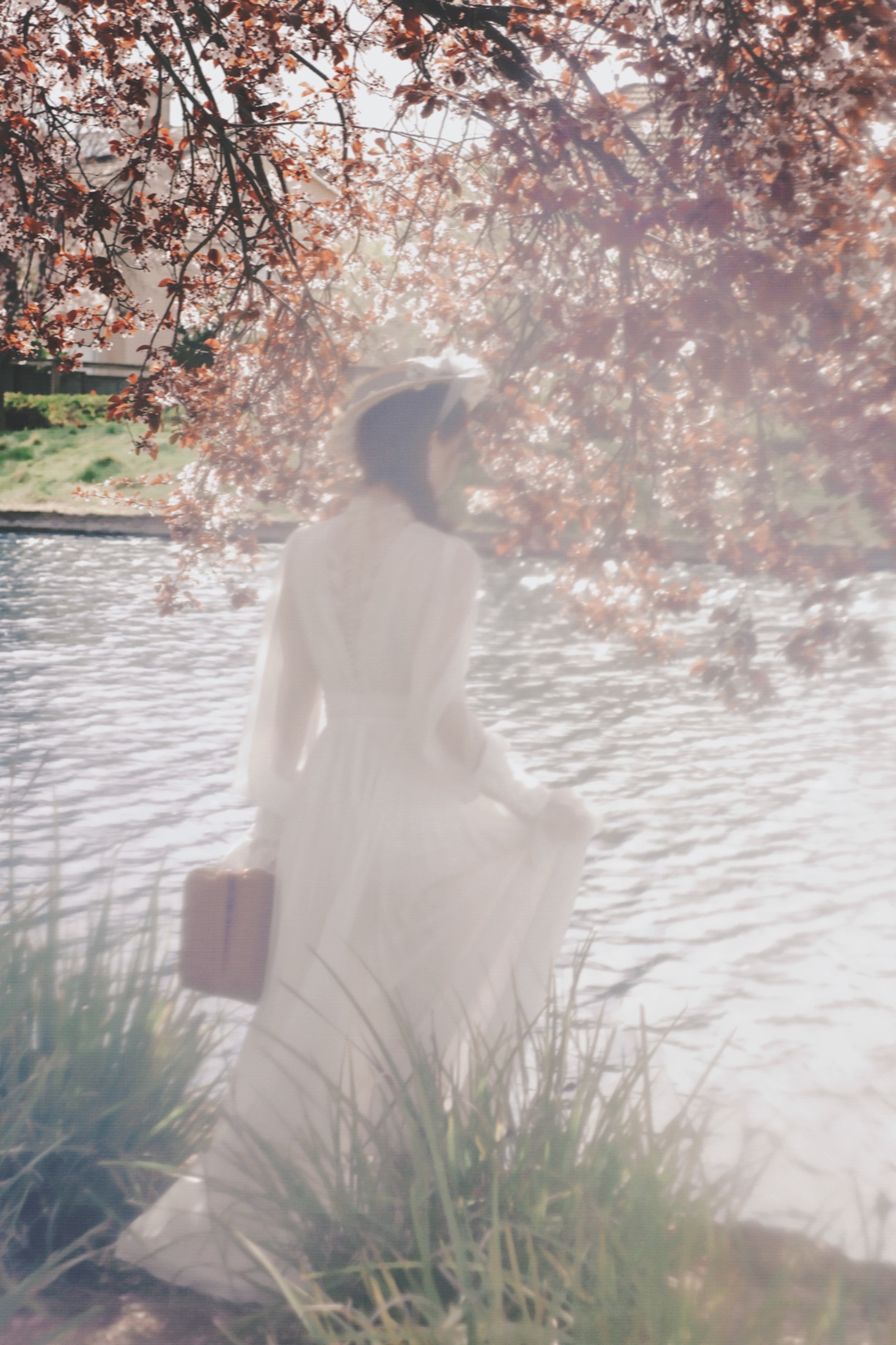 A woman in a white dress standing beside water and trees