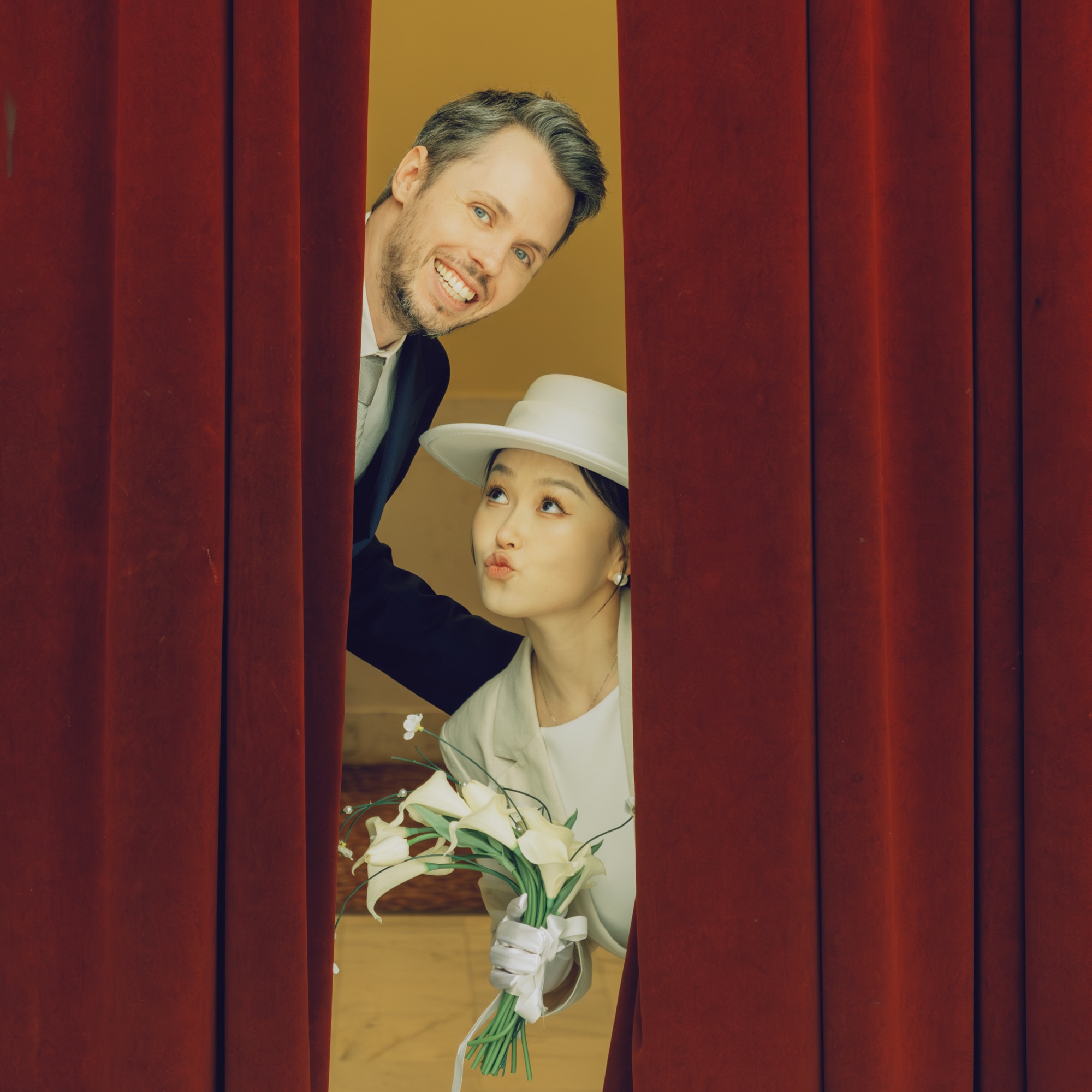 The couple smiling between red curtains